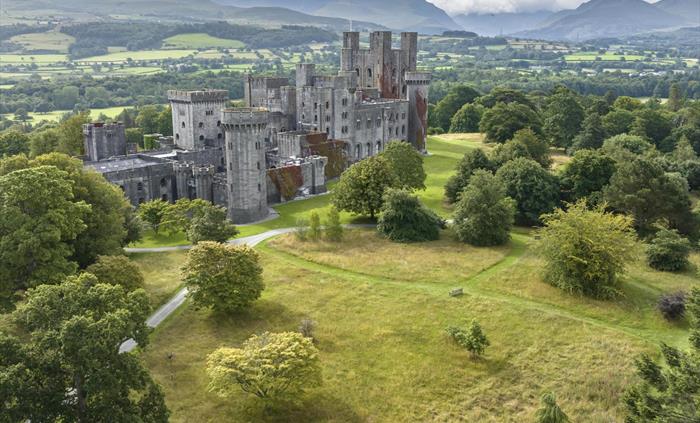 An aerial image of Penrhyn Castle surrounded by meadows with Eryri (Snowdonia) mountain range in the background.